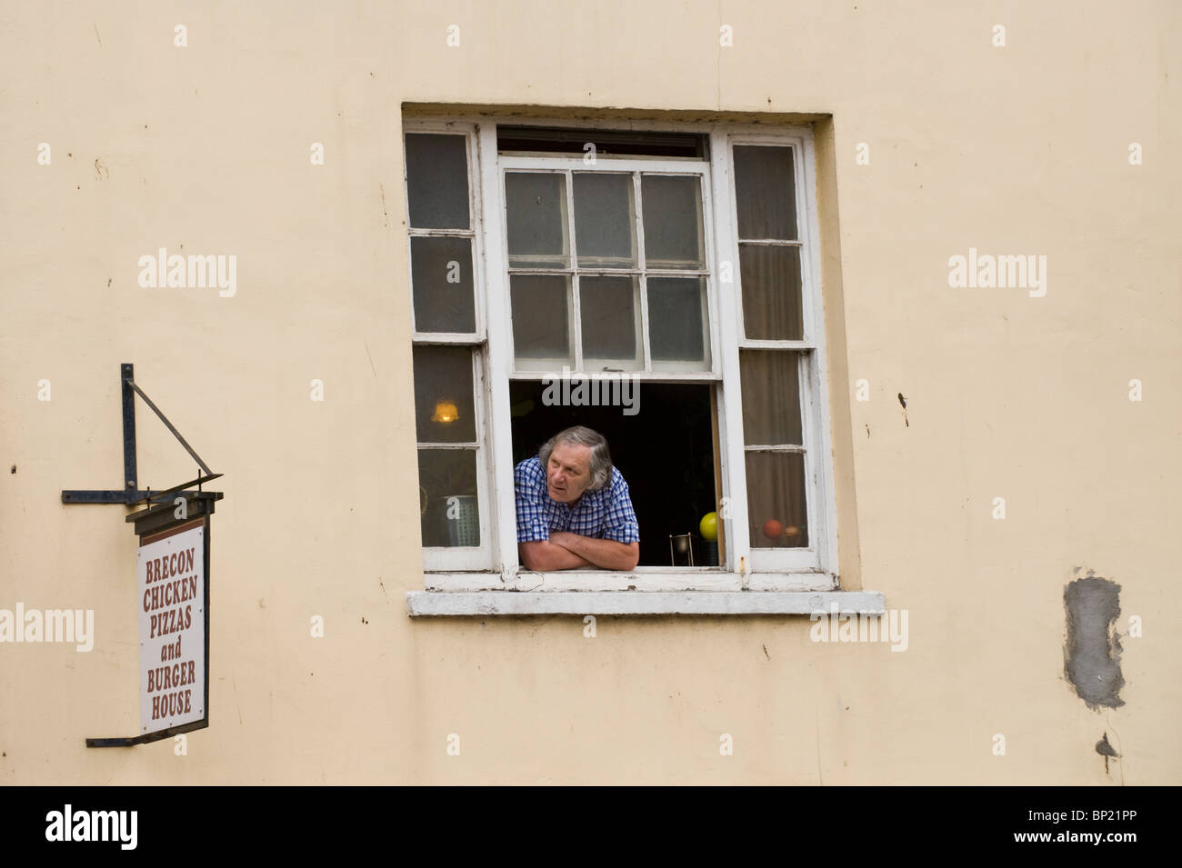Man looking out of open sash window watching parade through Brecon town during Brecon Jazz Festival 2010 Stock Photo