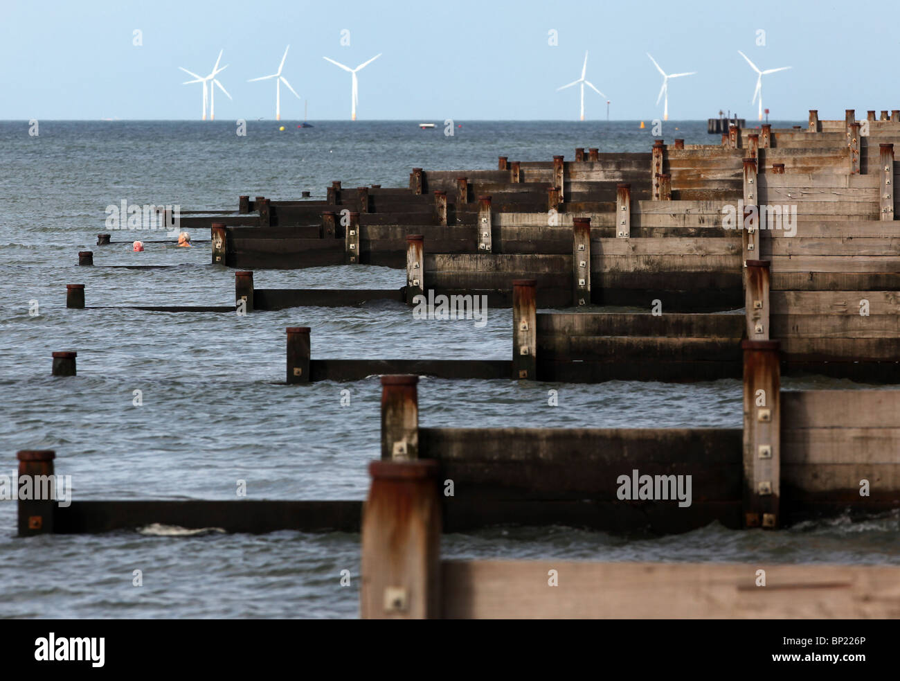 Groynes pictured alongside wind turbines in Whistable, Kent Stock Photo