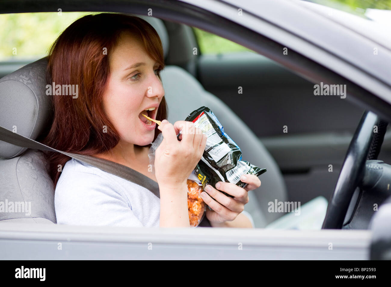 Woman snacking whilst driving Stock Photo