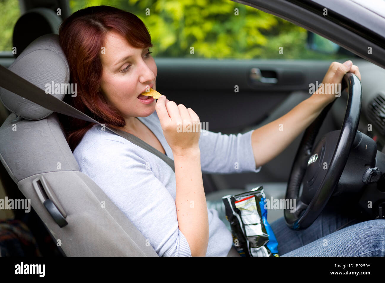 Woman snacking whilst driving Stock Photo