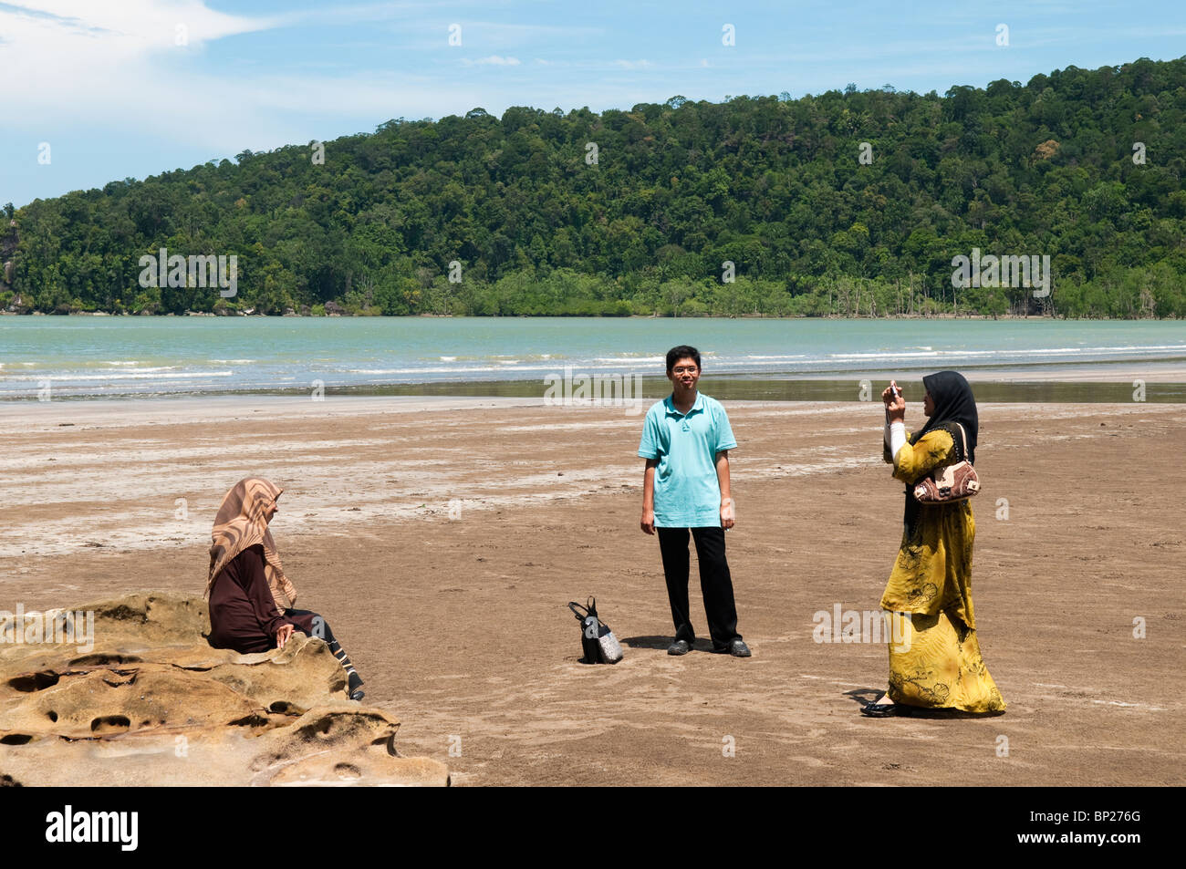 Malaysian tourists (Homo sapiens malayensis) taking pictures of each other on Telok Assam beach in Bako National Park. Stock Photo