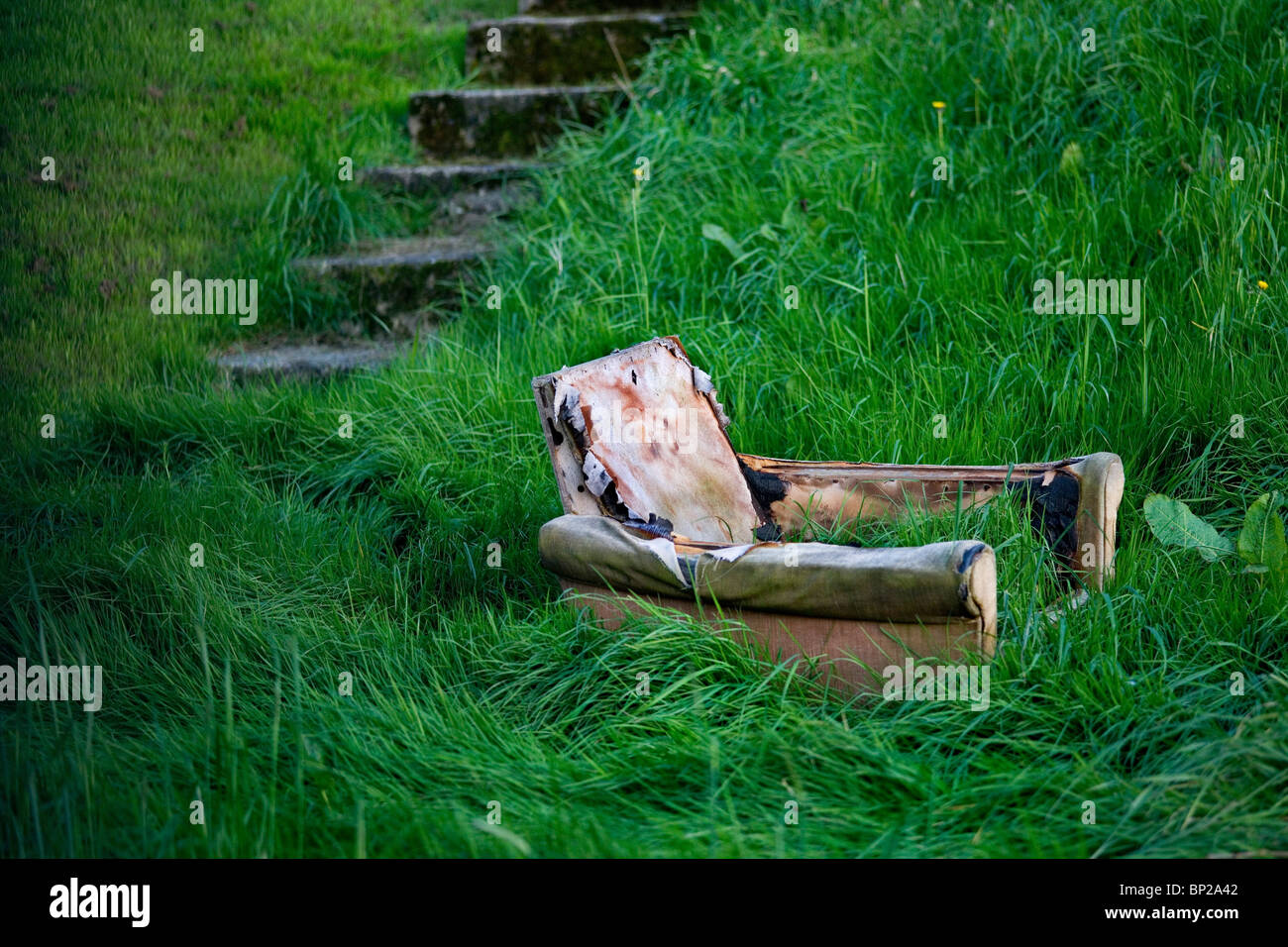 Abandoned sofa in London garden overgrown with grass Stock Photo