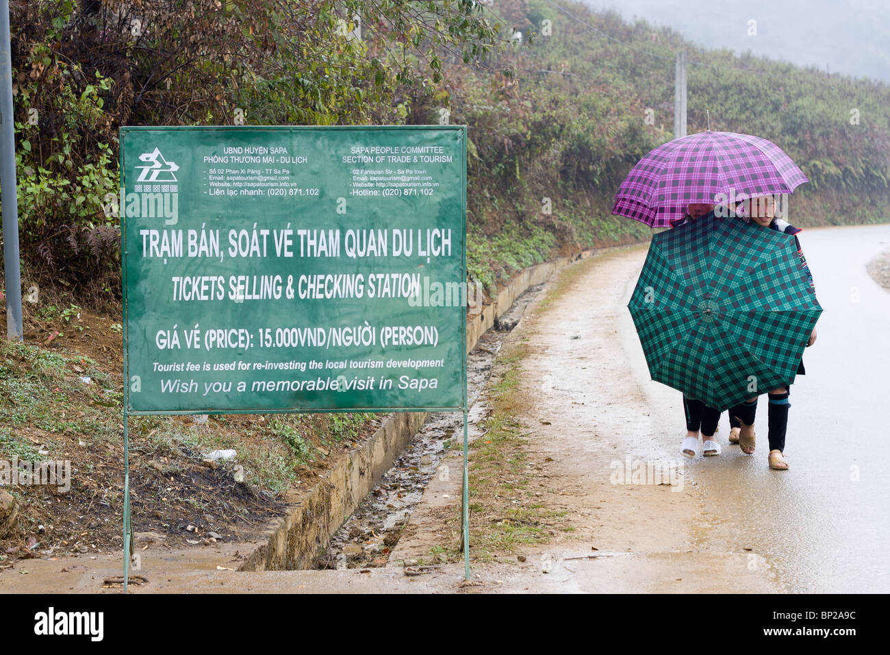 two black Hmong girls with two umbrellas try to stay dry while walking down the road. Stock Photo