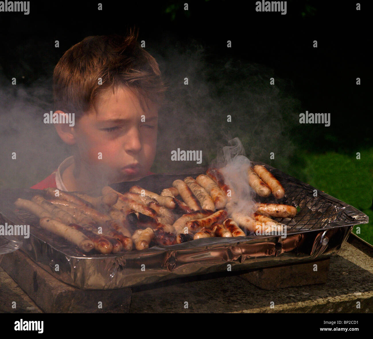 Boosting the heat, Boy blowing the charcoal in his barbecue to increase