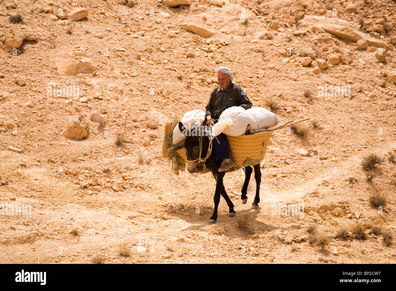 An Arab man rides a pack laden donkey on an arid hillside in Tunisia. Stock Photo