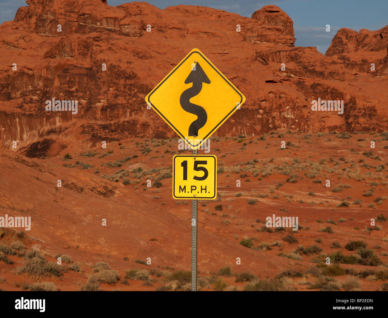 Desert curves ahead highway sign with cliff backdrop. Stock Photo