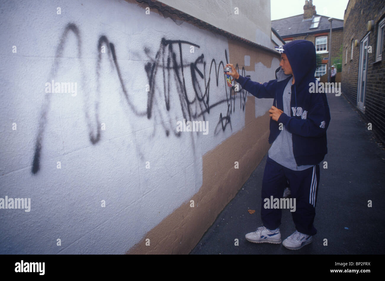 teenage boy defacing a wall with graffiti Stock Photo