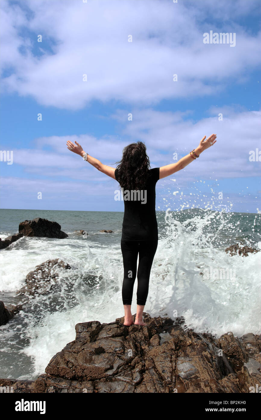 a beautiful woman doing yoga on the edge of the rocks with waves splashing to show a healthy way to live a happy  life Stock Photo