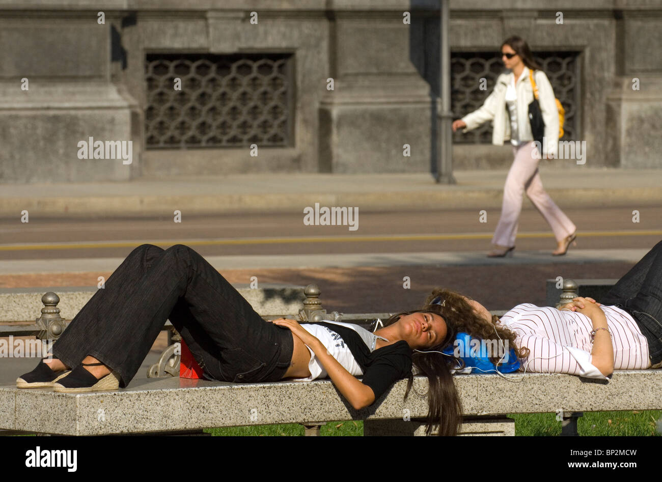 Young girls relaxing on a bench and listening to music, Milan, Italy Stock Photo