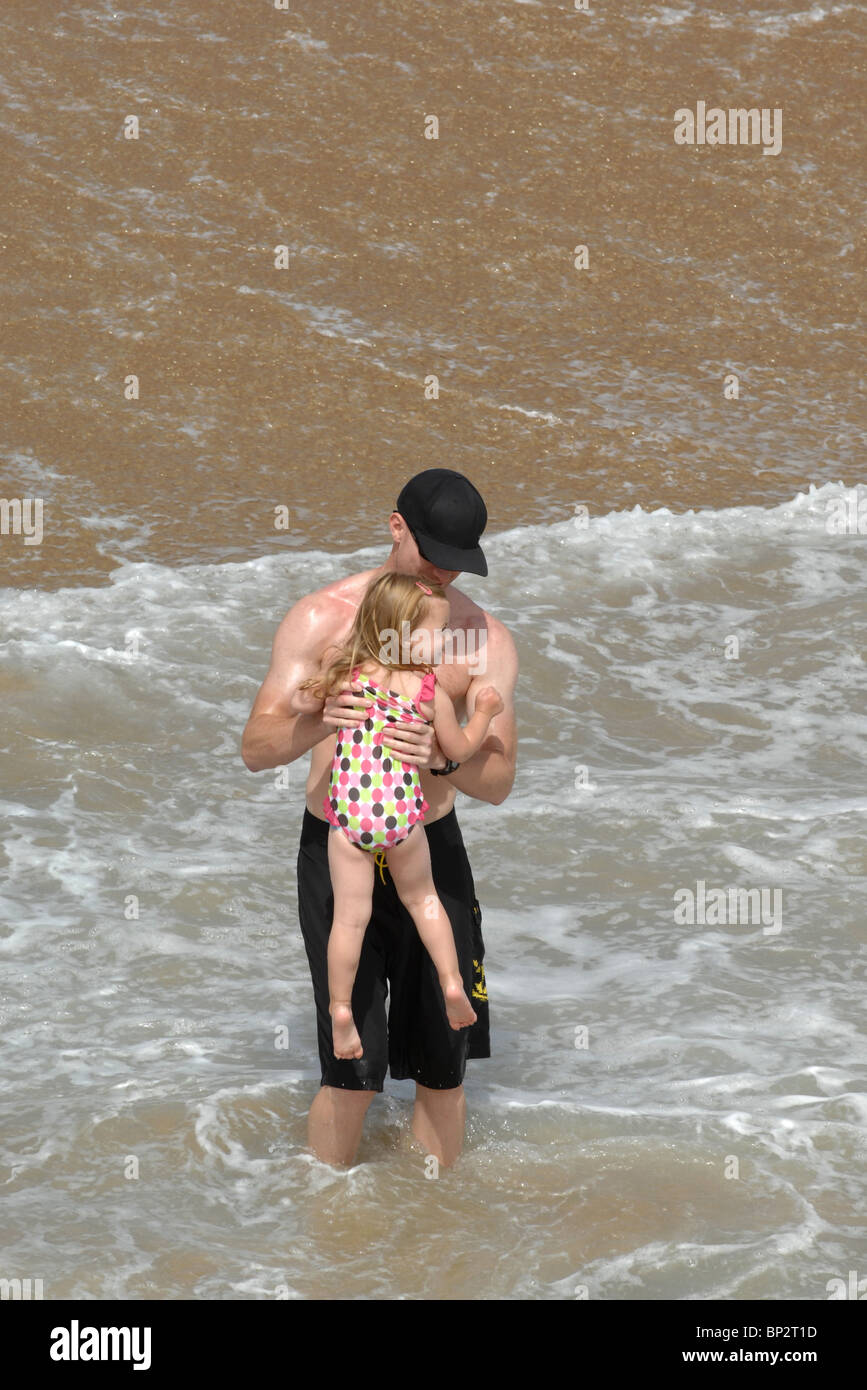 An attractive athletic man plays with his daughter in the waves at the ocean. Stock Photo