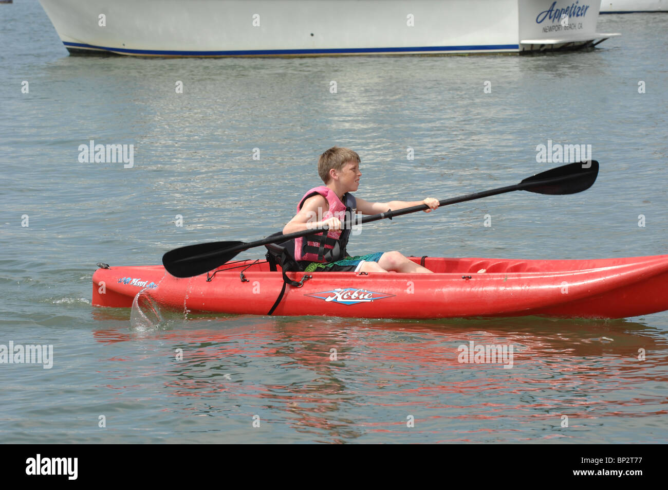 Young white boy paddling on a red kayak. Stock Photo