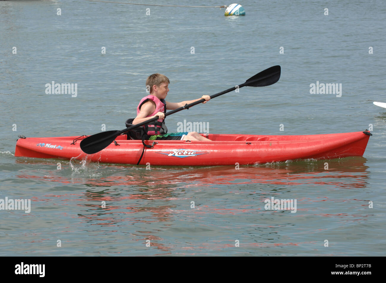 Young white boy paddling on a red kayak. Stock Photo