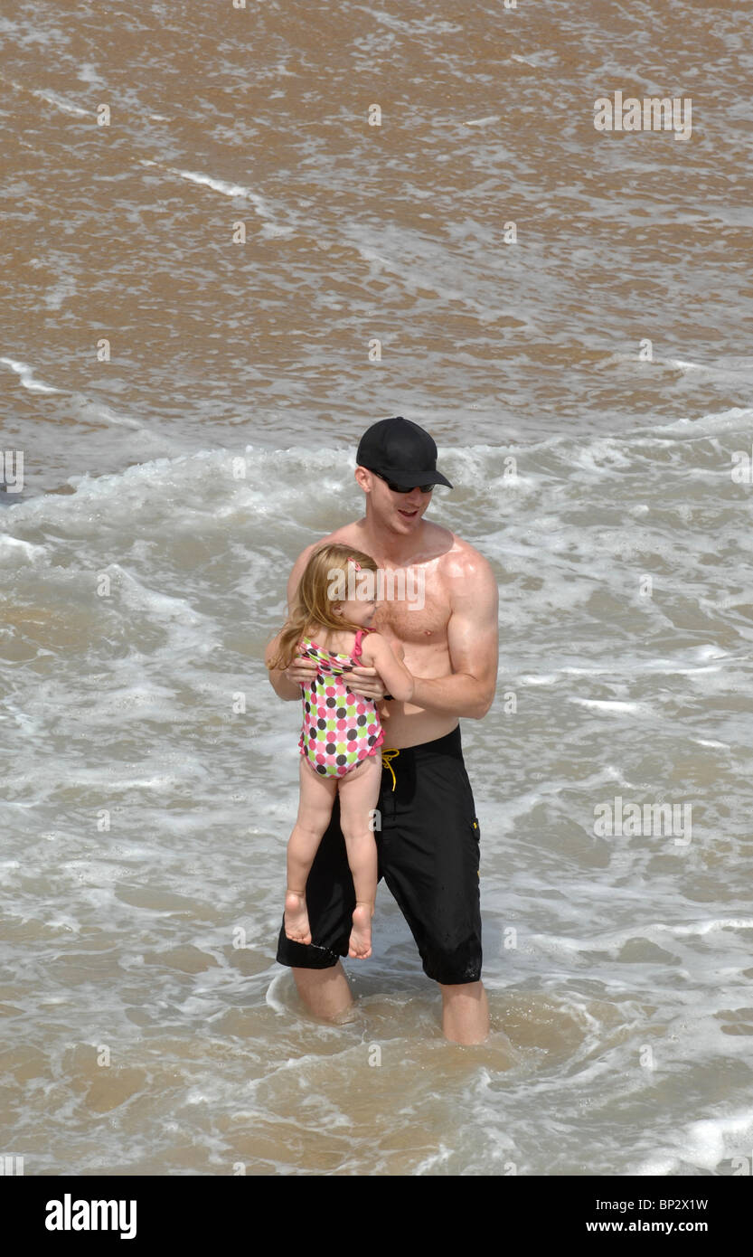 An attractive athletic man plays with his daughter in the waves at the ocean. Stock Photo