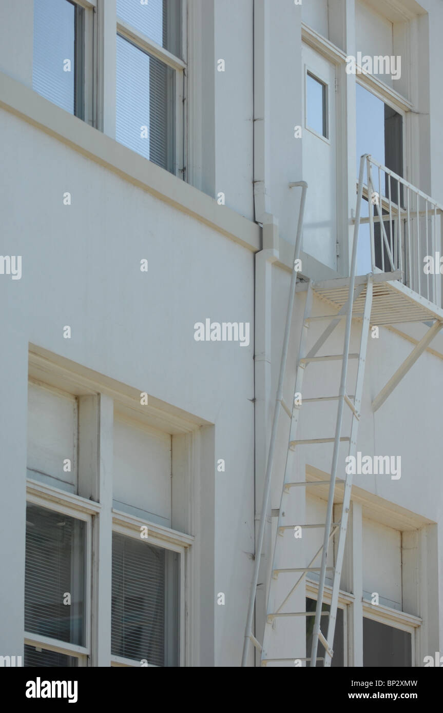 Emergency exit ladder and stairs painted white to match the side of a clean white building. Stock Photo