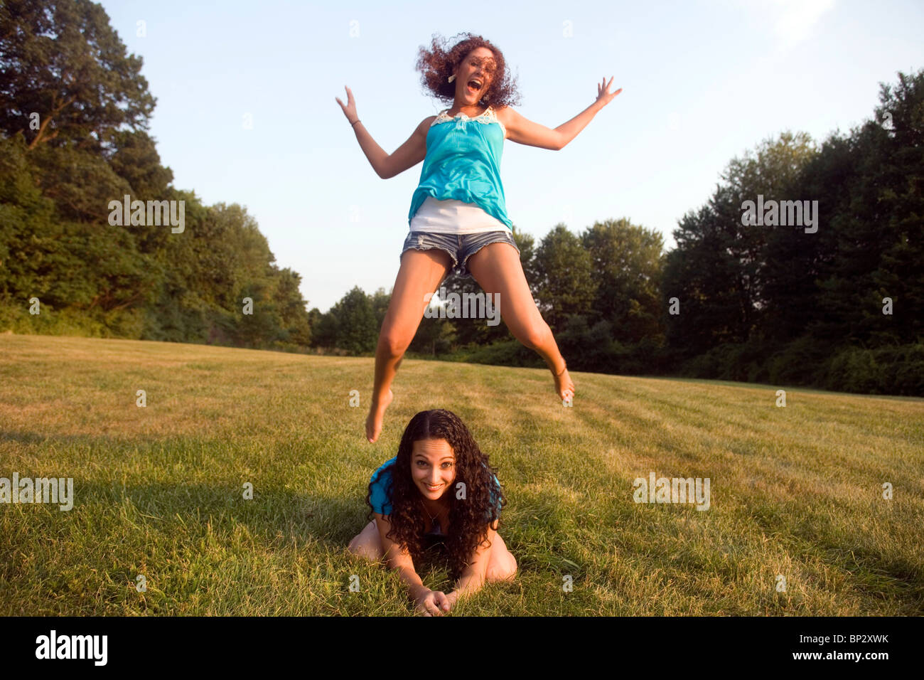 Two early twenties caucasian females play leap frog on a clear afternoon in a Connecticut, USA, meadow. Stock Photo