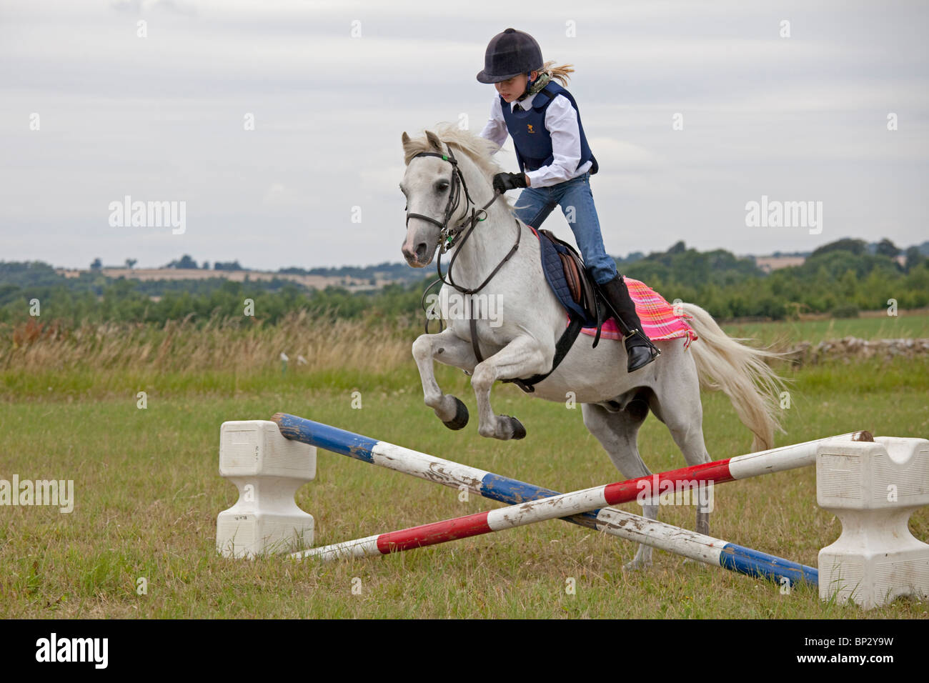 Young girl white horse jumping competition gymkhana pony club camp North Cotswolds UK Stock Photo