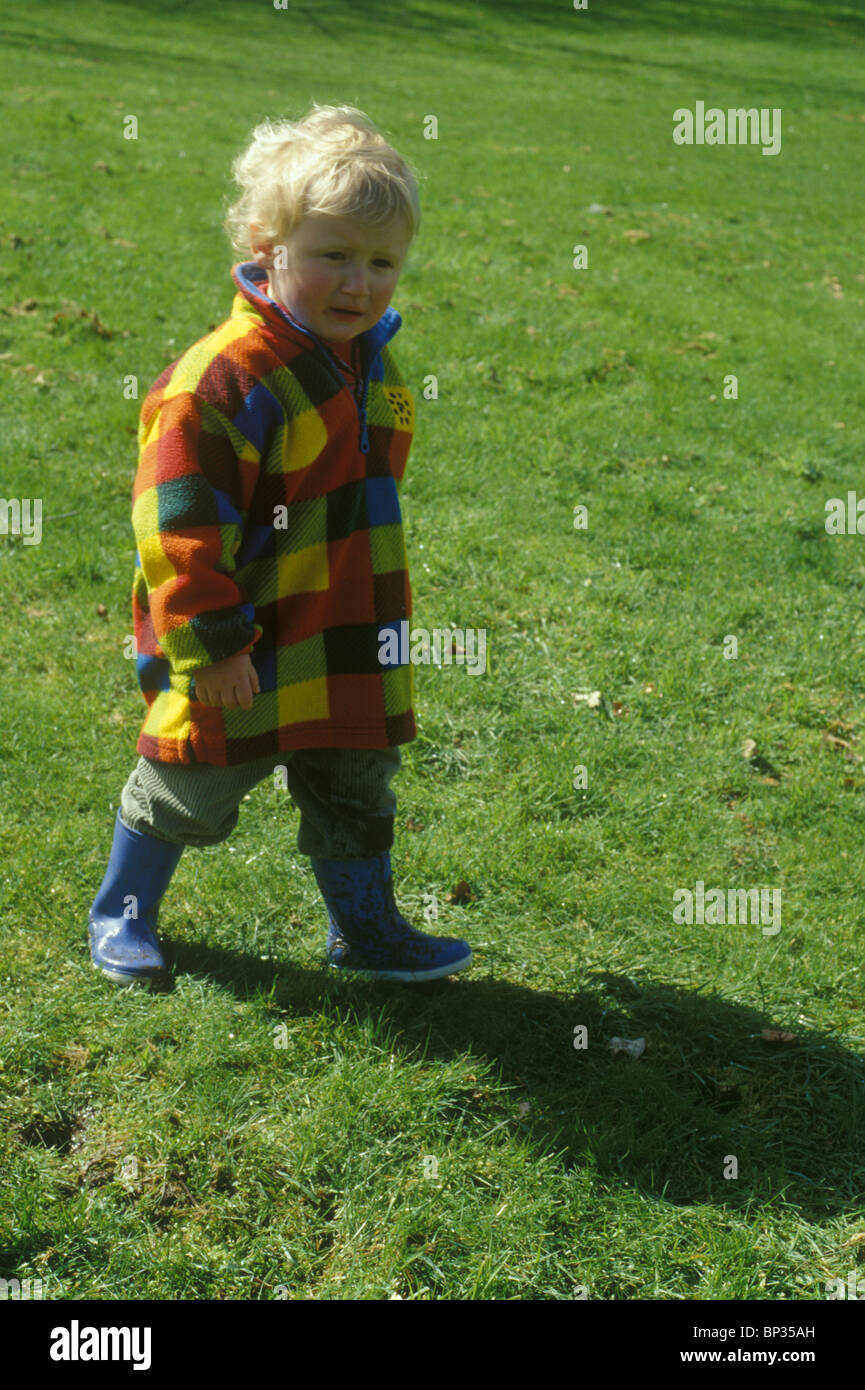 toddler walking on grass looking miserable Stock Photo