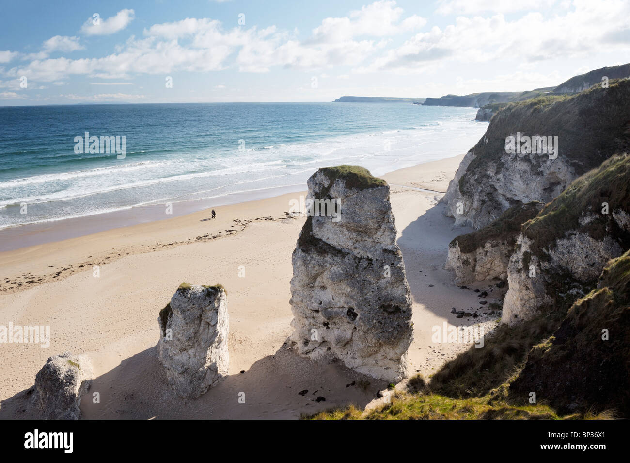 Couple walking alone on beach at the White Rocks between Portrush and Bushmills, Northern Ireland. Eroded limestone cliffs Stock Photo