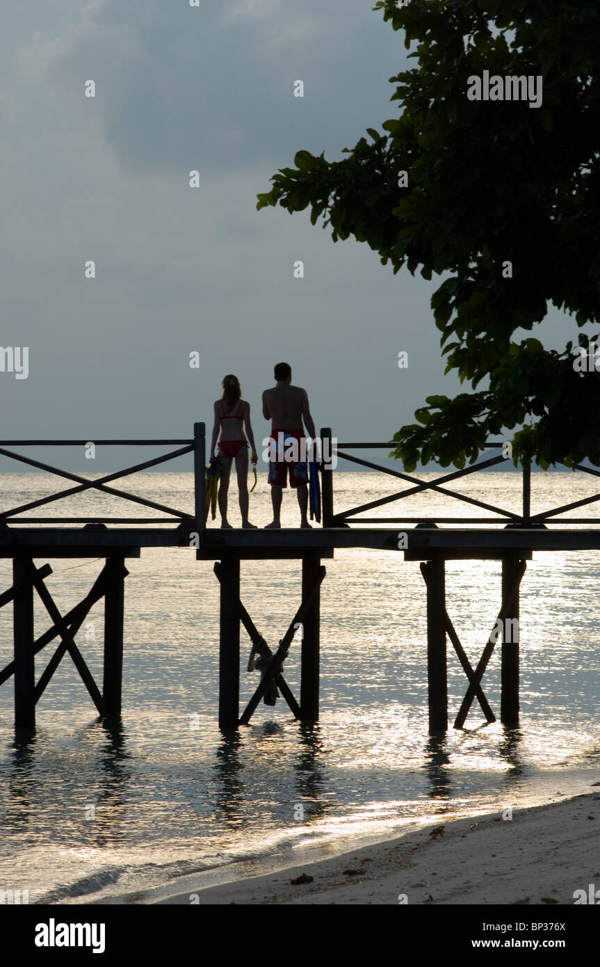 Couple on jetty with snorkel gear at sunset, Pom Pom Island Resort, Celebes Sea, Sabah, East Malaysia. Stock Photo