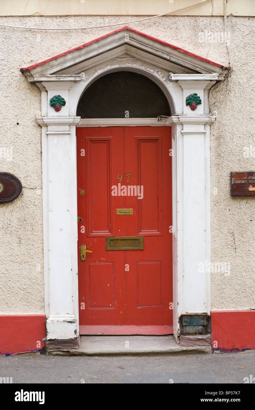 Red wooden paneled front door no. 97 with brass letterbox and white triangular pediment architrave of Georgian town house in UK Stock Photo