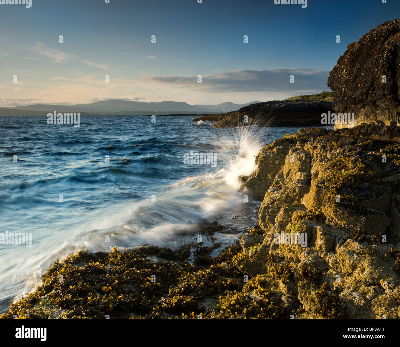 Waves breaking on rocky shore in the evening light Stock Photo
