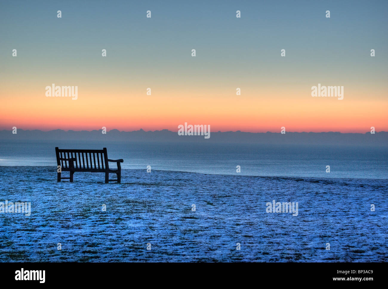 An empty chair facing out to sea on a very cold January morning. Ice on the ground. Sunrise. Stock Photo