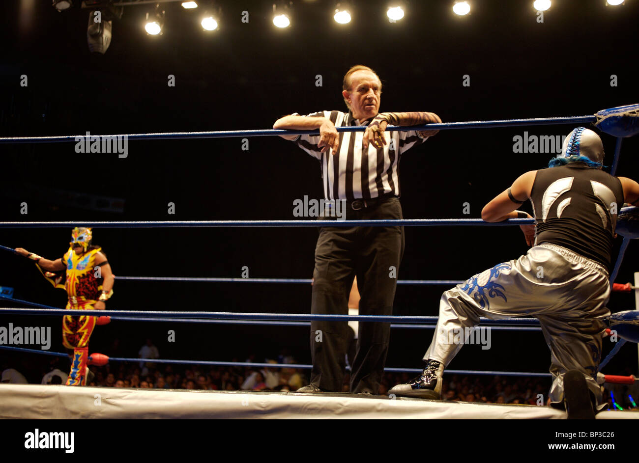A referee looks at wrestlers during a fight at a Lucha Libre Wrestling