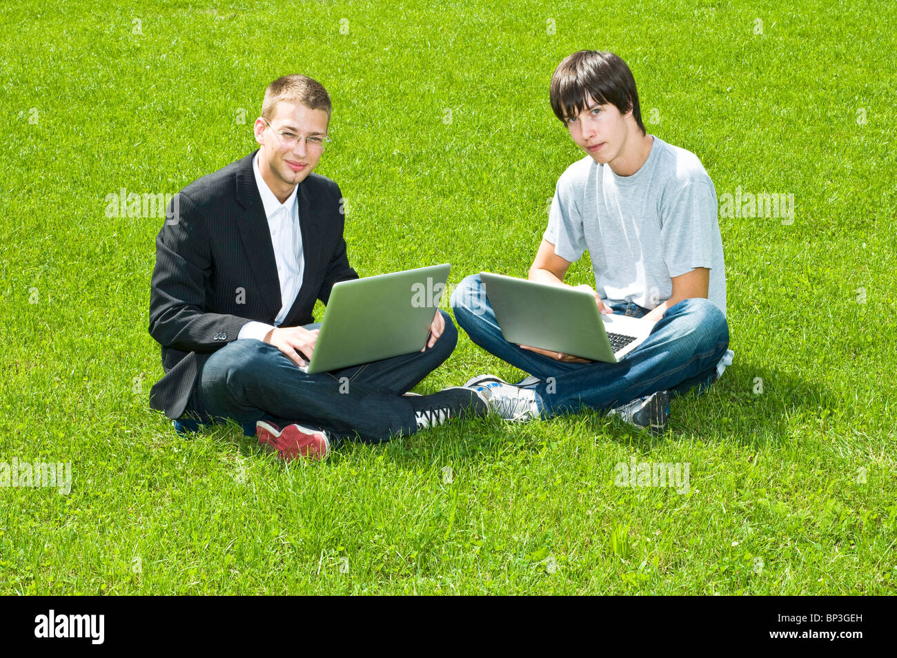 Two young men sitting with their laptops on green grass resting Stock ...