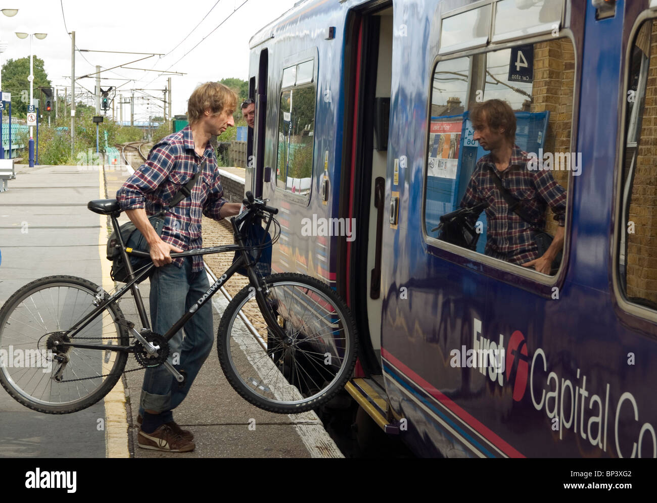 The train driver looks on as a cyclist loads his bicycle onto a First Capital Connect train at Finsbury Park Station, London Stock Photo