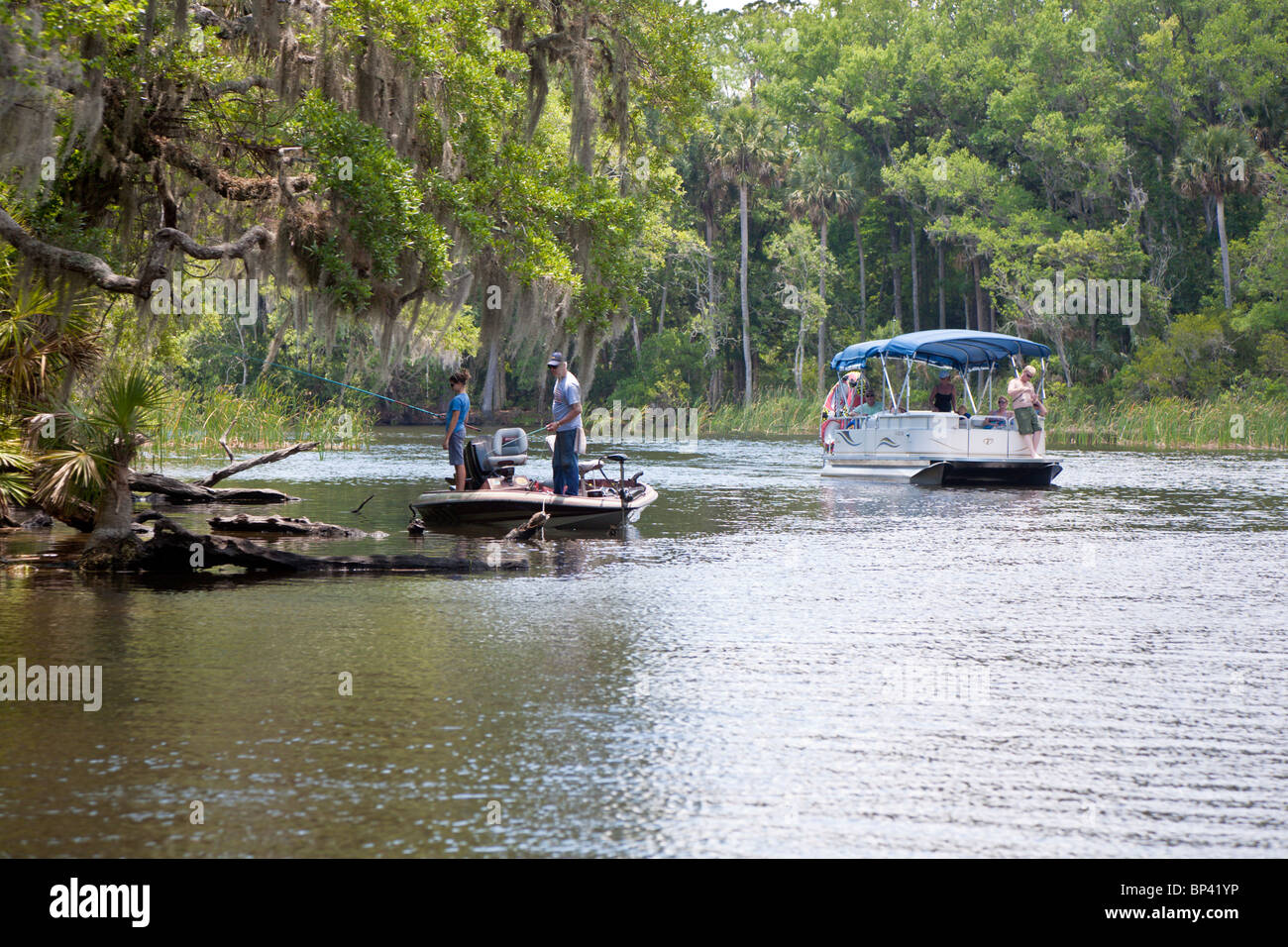 Family in a pontoon boat passes a young girl fishing with her grandfather on the Salt River in central Florida Stock Photo