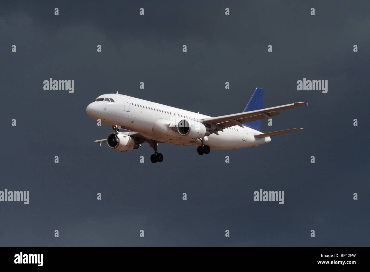 Airbus A320 passenger jet plane flying on approach in a dark cloudy sky. No livery and proprietary details deleted. Commercial air travel, aviation. Stock Photo