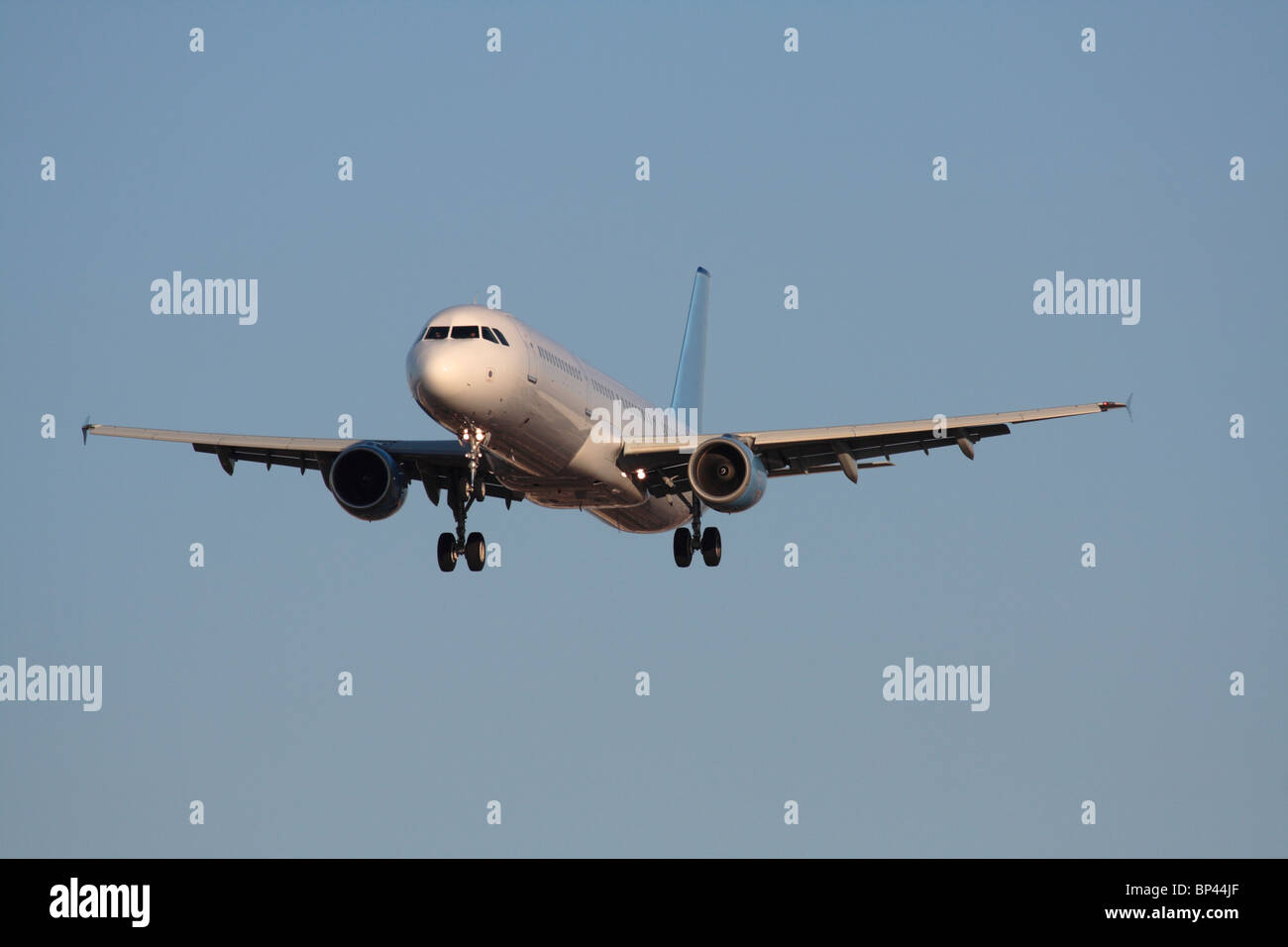 Air travel. Airbus A321 narrowbody commercial passenger jet plane flying on approach in a blue sky. Front view with proprietary details deleted. Stock Photo