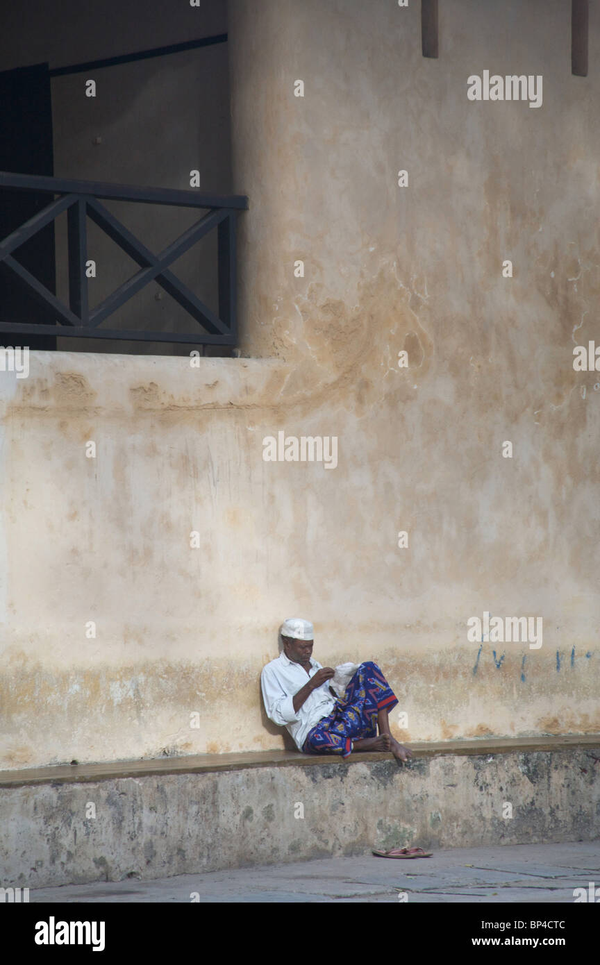 A man sits in Lamu's main square in front of the old fort, Kenya, Africa Stock Photo