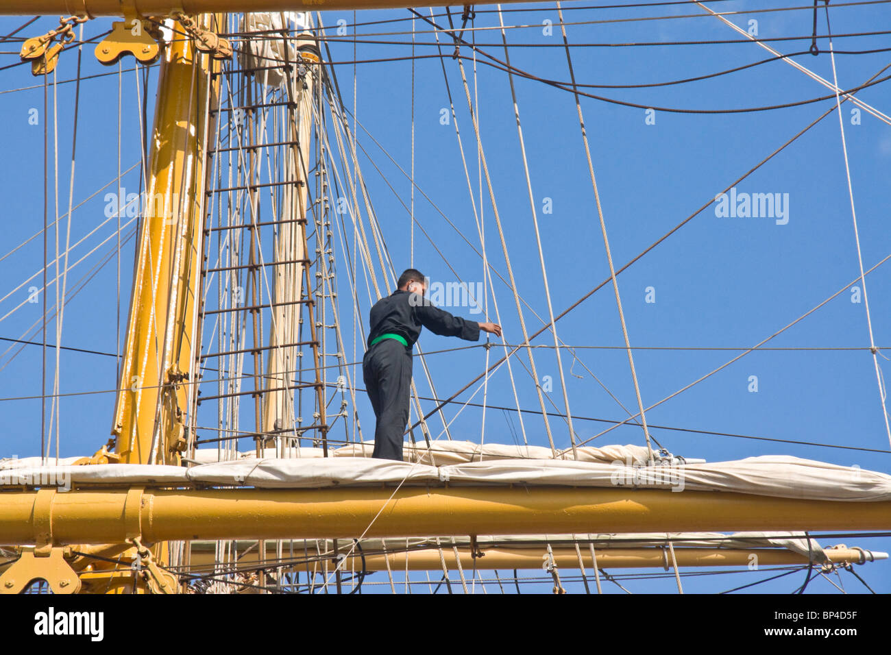Member of the crew of a barquentine rigged sailing ship working on the middle yard (spar) of the foremast and rigging. Stock Photo