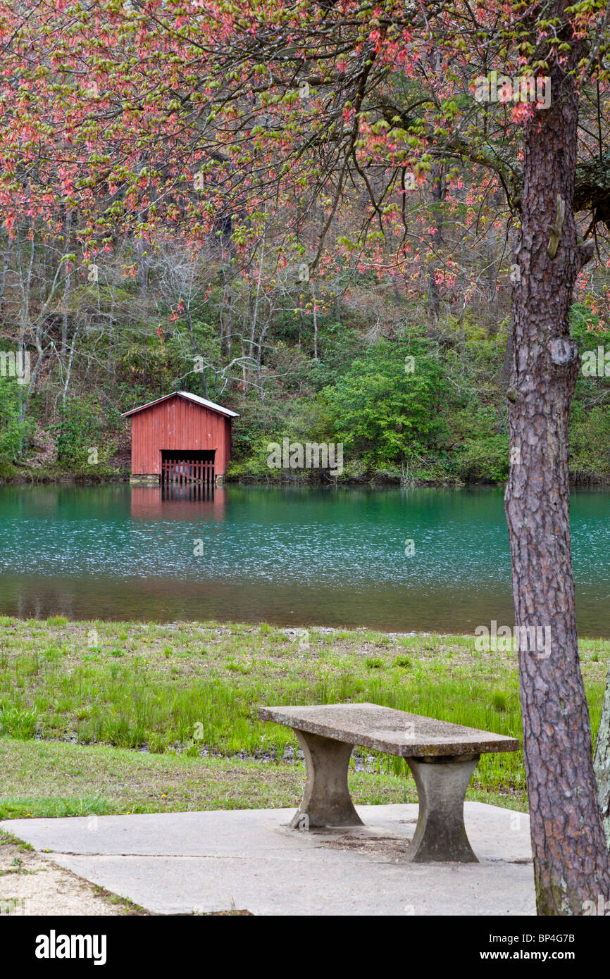 Red boathouse across river from concrete bench under blooming tree in