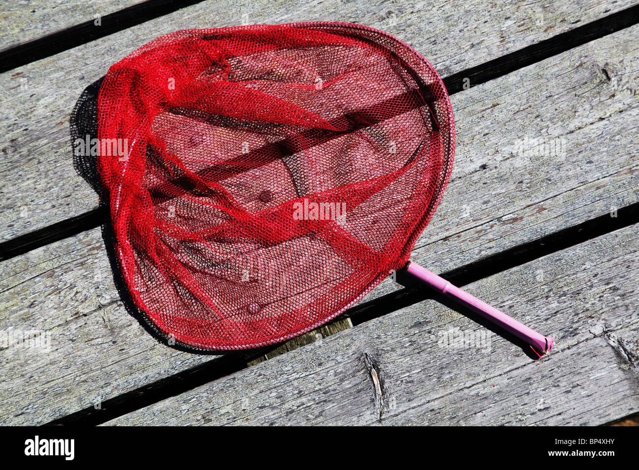 Bright pink red child's fishing or butterfly net lying on a wooden pier Stock Photo