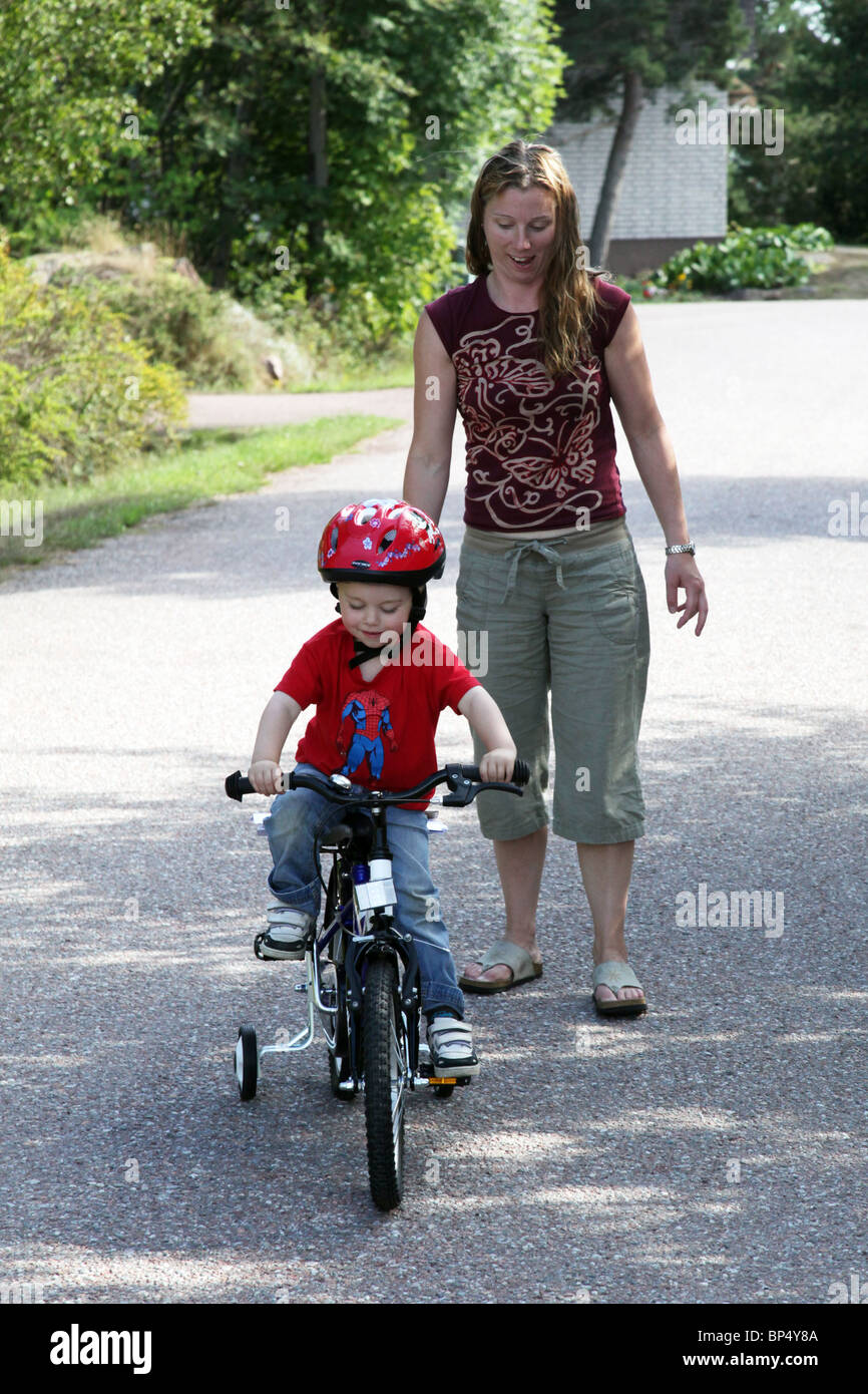 Little boy toddler riding his first bicycle lesson with his mum with stabilisers MODEL RELEASED Stock Photo