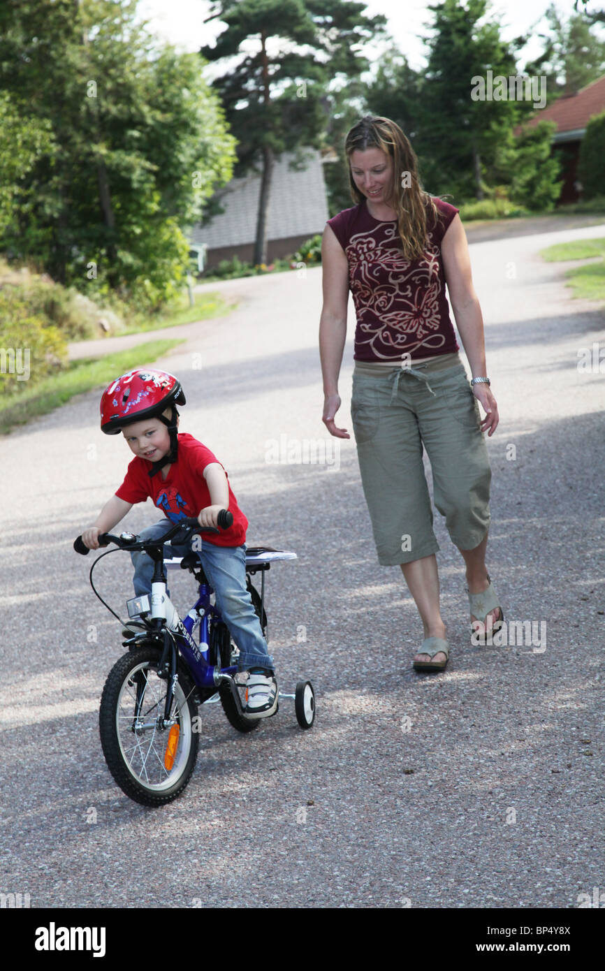 Little boy toddler riding his first bicycle lesson with his mum with stabilisers MODEL RELEASED Stock Photo