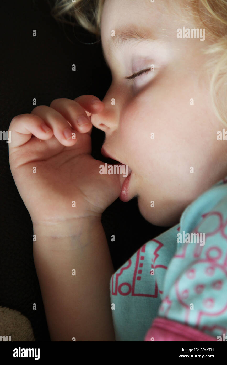 Toddler child girl sleeping taking a nap in the afternoon on a sofa sucking her thumb MODEL RELEASED Stock Photo
