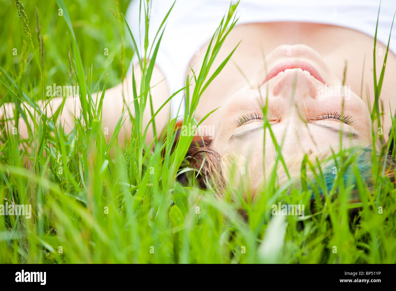 Young woman laying on a grass field relaxing and smiling. Stock Photo