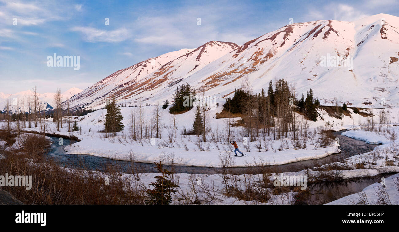 COMPOSITE Female cross country skiing in Turnagain Pass at sunrise with Bertha Creek in the foreground, Southcentral, Alaska Stock Photo