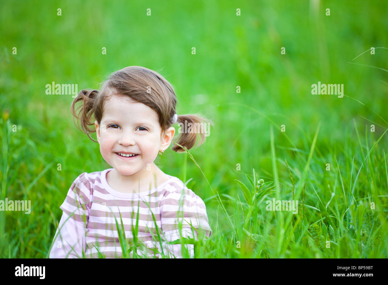 Portrait of a little girl sitting in the grass smiling happily Stock ...