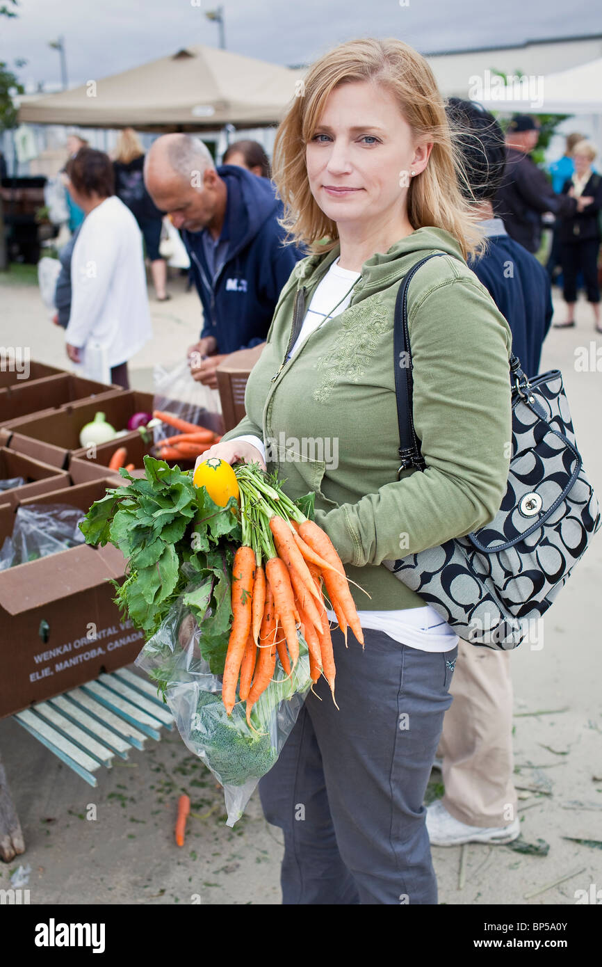 Woman holding fresh carrots at an outdoor farmers market, St. Norbert Farmers Market, Winnipeg, Manitoba, Canada. Stock Photo