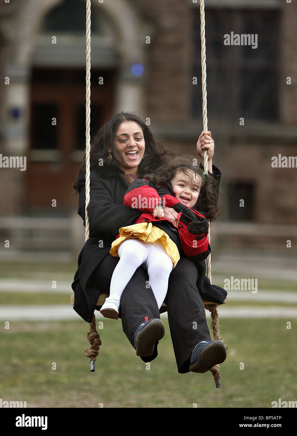 A mother and daughter laugh as they swing on a rope-swing at Yale University in New Haven, CT USA Stock Photo