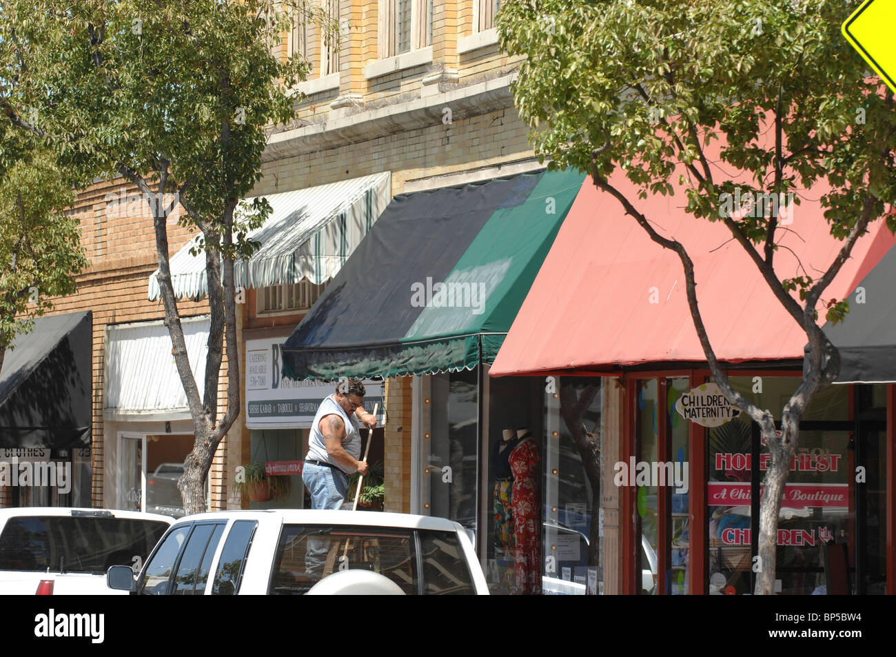 A man on a ladder painting a green awning over the storefront window. Stock Photo