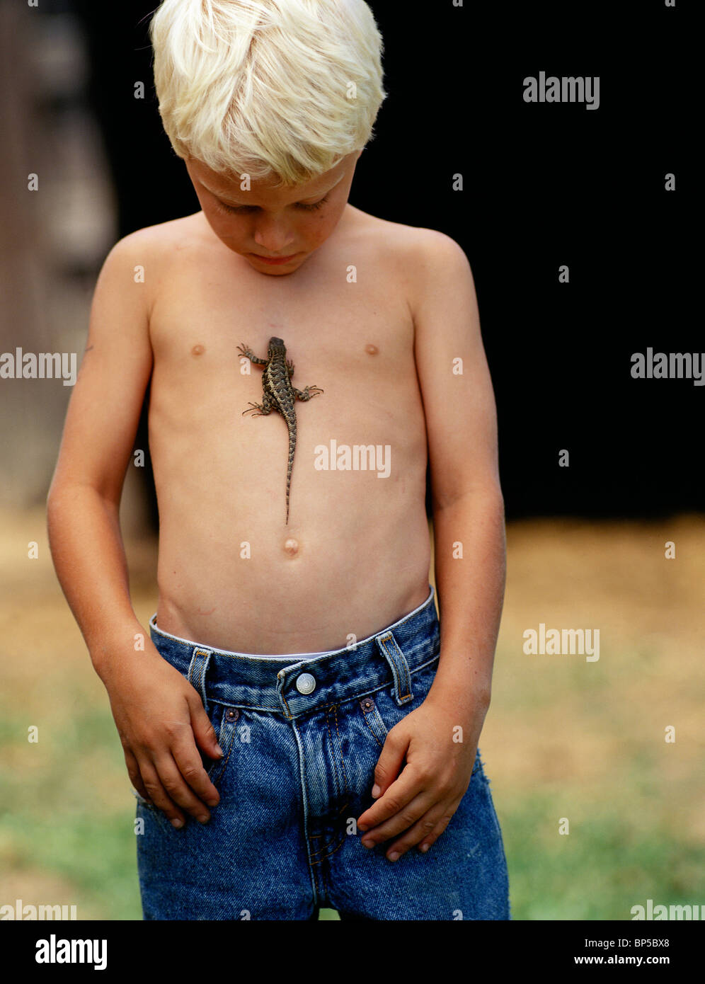 Caucasian boy in jeans with a lizard running up his chest. Stock Photo