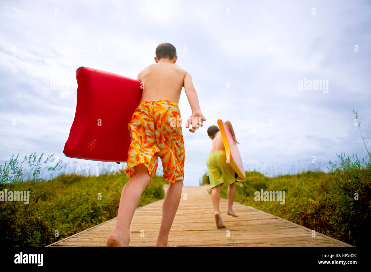 Two boys in swimming suits running on a beach boardwalk. Stock Photo