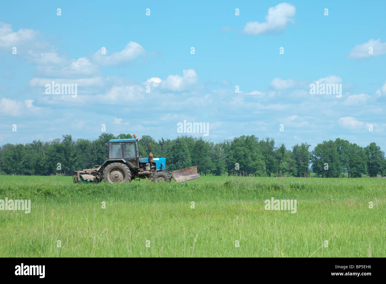 The old tractor goes through a green field Stock Photo - Alamy