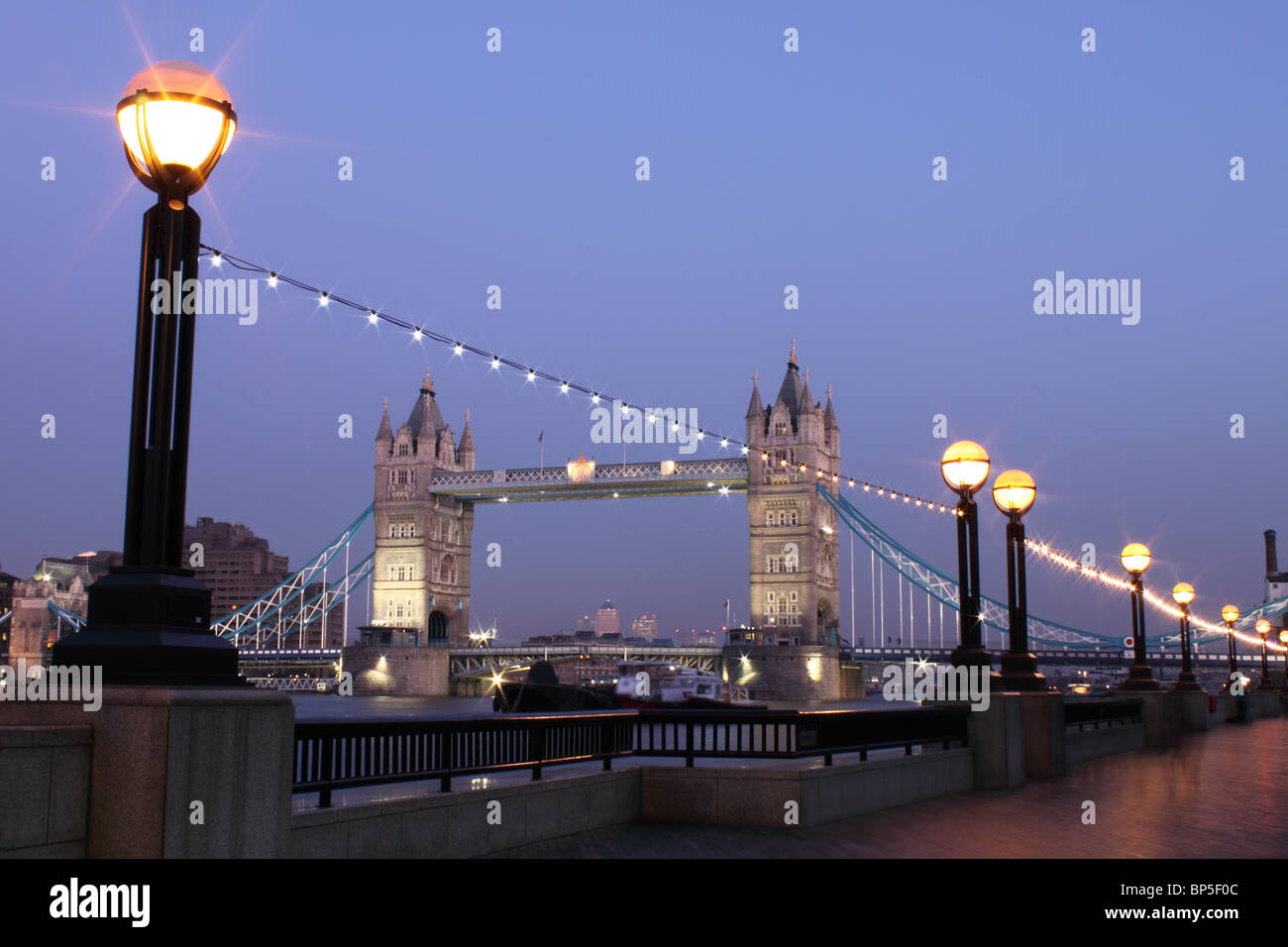 Tower Bridge at dusk from the South bank, with embankment lights in foreground and lights on bridge, London, England, UK Stock Photo
