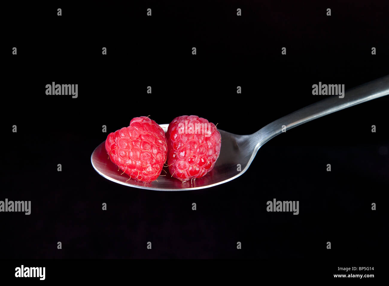 Fresh raspberries on spoon with black background. Stock Photo